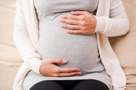 Waiting for a baby. Close-up of young pregnant woman touching her abdomen while sitting on the couch