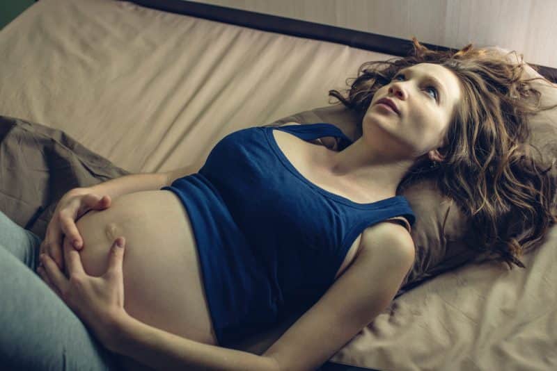 pregnant woman in bed holding stomach